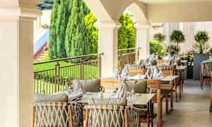 Uteservering med dukade bord och stolar i en grönskande miljö. (AI-genererad text)