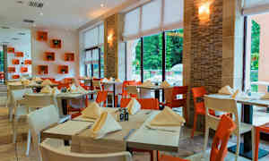 Fotografi av en inomhusrestaurang med dukade bord och stolar i olika färger. (AI-genererad text)