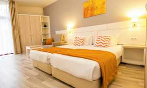 Ett ljust hotellrum med två sängar, orange detaljer och möbler. (AI-genererad text)