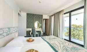 Hotellrum med ljusa möbler och stora fönster med utsikt över havet. (AI-genererad text)