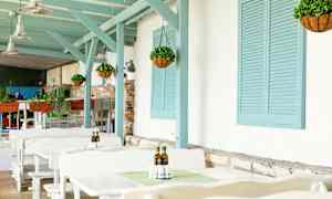 Utomhus sittområde med vita bord, hängande växter och blå trädetaljer. (AI-genererad text)