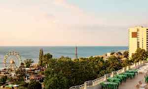 Bilden visar en kust med hav, ett pariserhjul, grönskande träd och byggnader. (AI-genererad text)