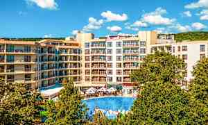 Ett hotellområde med flervåningsbyggnader, en stor utomhuspool och gröna träd i förgrunden. (AI-genererad text)