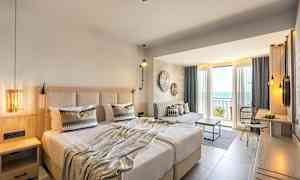 Hotellrum med dubbelsäng, sittplats och balkong med utsikt över havet. (AI-genererad text)