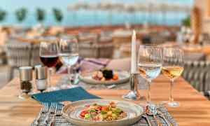 En dukad restaurangbord med en tallrik mat och glas med vin, vatten och ett tänt ljus. (AI-genererad text)