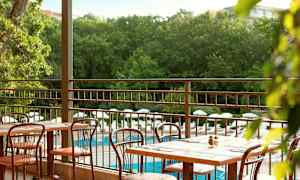 Uteservering med bord och stolar samt utsikt över poolområde och grönska. (AI-genererad text)