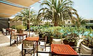 En uteservering med bord och stolar nära en pool med omgivande palmer. (AI-genererad text)