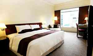 Hotellrum med en stor säng, ett skrivbord och en fåtölj bredvid ett stort fönster. (AI-genererad text)