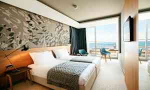 Ett modernt hotellrum med två enkelsängar, en väggdekoration, och en balkong med utsikt över havet. (AI-genererad text)