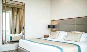 Ett hotellrum med en stor säng, kuddar och en spegel. (AI-genererad text)