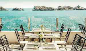 En restaurangterrass med havsutsikt, bord och stolar står uppställda med dukning. (AI-genererad text)