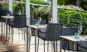 En uteservering med bord och stolar uppdukade med glas och servetter. (AI-genererad text)