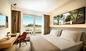 Hotellrum med en säng, skrivbord och stol, samt en balkong med utemöbler. (AI-genererad text)