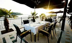 Uteservering med bord och stolar, med havsutsikt och solnedgång. (AI-genererad text)