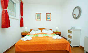 Ett sovrum med en dubbelsäng och orange överkast, två sidobord med lampor samt väggdekorationer. (AI-genererad text)