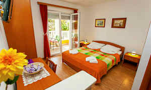 Ett rum med en dubbelsäng, bord, stolar och en öppnad balkongdörr. (AI-genererad text)