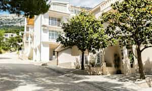 Vit byggnad med flera våningar och balkonger, omgiven av grönska. (AI-genererad text)