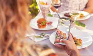 Person tar foto av tallrik med mat på utomhusbord. (AI-genererad text)