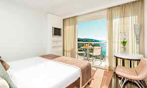 Hotellrum med en stor säng som vetter mot en balkong med utsikt över havet. (AI-genererad text)