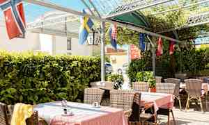 Utomhusterrass med bord, stolar och flaggor, omgiven av grönska. (AI-genererad text)