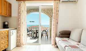 Ett vardagsrum med en bäddsoffa, ett kök och en balkong med utsikt över havet. (AI-genererad text)