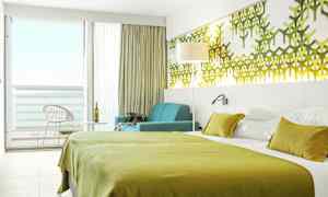 Ett hotellrum med en grön sängklädsel, väggdekorationer och en sittgrupp vid ett fönster mot balkongen. (AI-genererad text)