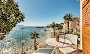 Utsikt från en balkong mot en solig strand med palmer och klart vatten. (AI-genererad text)