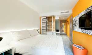 Ett modernt hotellrum med en stor säng klädd i vita sängkläder, orange och vita väggar, en väggmonterad TV och ett skrivbord. (AI-genererad text)