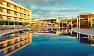 En pool omgiven av solstolar och parasoller intill en byggnad och en restaurang. (AI-genererad text)