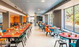 En modern matsal med stora fönster, färgglada stolar och dukade bord. (AI-genererad text)