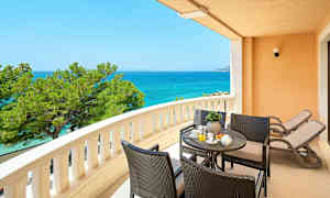 En balkong med utsikt över havet, sittgrupp och två solstolar. (AI-genererad text)