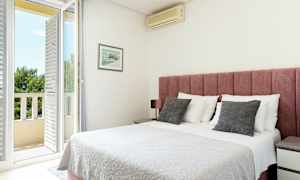 Ett ljust sovrum med en rosa sänggavel, vitt sängöverkast, och en dörr till en balkong. (AI-genererad text)