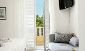 Ett hotellrum med en soffa, en säng och en balkongdörr som leder ut till en utsikt över träd. (AI-genererad text)