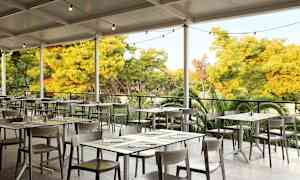 En utomhusrestaurang med bord och stolar under ett tak, omgiven av grönska. (AI-genererad text)