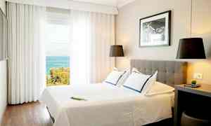 Ett ljust hotellrum med en dubbelssäng, modern inredning och havsutsikt genom stora fönster. (AI-genererad text)