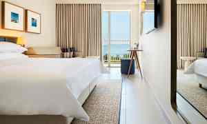 Hotellrum med bäddad säng, soffa, och balkong med havsutsikt. (AI-genererad text)