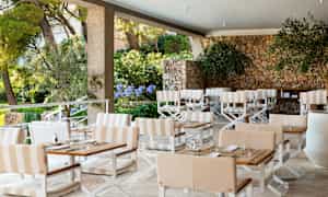 En utomhusterrass med bord, stolar och en stenmur. (AI-genererad text)