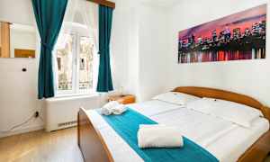 Ett sovrum med dubbelsäng, turkosa gardiner och en bild av en stadssiluett på väggen. (AI-genererad text)