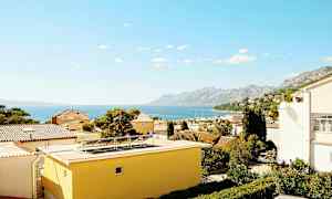 Utsikt över hustak med havet och berg i bakgrunden. (AI-genererad text)