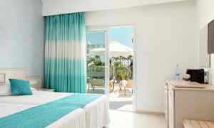 Ljust hotellrum med dubbelbädd och utsikt mot en terrass med solstolar och parasoller. (AI-genererad text)