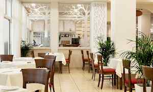 En restaurang med bord och stolar, dekorerad med växter och en glasvägg med ett trädesignmotiv. (AI-genererad text)