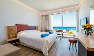 Hotellrum med en dubbelsäng, sittgrupp och utsikt över havet. (AI-genererad text)