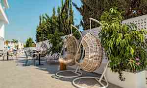 Hängande korgstolar och bord på en terrass med växter och parasoller. (AI-genererad text)