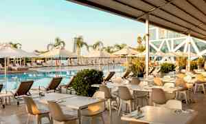 Poolområde med solstolar, parasoller och matbord vid vattnet. (AI-genererad text)