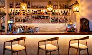 En bardisk med stolar och hyllor fyllda med flaskor och glas. (AI-genererad text)