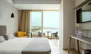 Ett hotellrum med modern inredning, en bred säng, en gul sittstol, ett bord med utsikt över stranden genom stora fönster. (AI-genererad text)