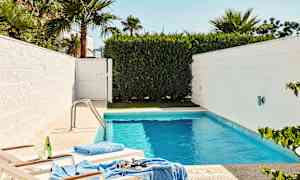 En mindre pool omgiven av vita väggar och grön vegetation, med två solstolar nära vattenkanten. (AI-genererad text)