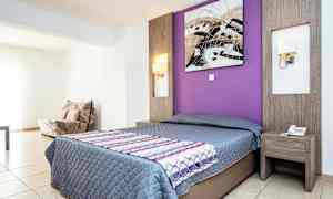 Ett hotellrum med en dubbelsäng, ett lila vägg bakom sängen och ett sidobord. (AI-genererad text)