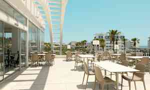 Uteservering med bord och stolar under en öppen struktur med utsikt mot palmer och byggnader. (AI-genererad text)