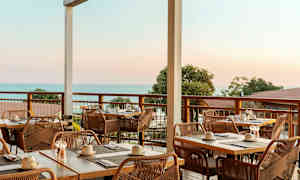 Uteservering med dukade bord och utsikt mot havet. (AI-genererad text)